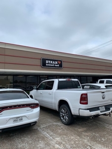 A white Dodge Charger and a white Dodge Ram truck are parked in front of a building