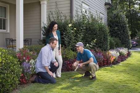A couple and a gardener are examining the landscape in front of a house.