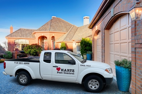 A white Hartz Pest Control truck is parked in front of a brick house with a garage.