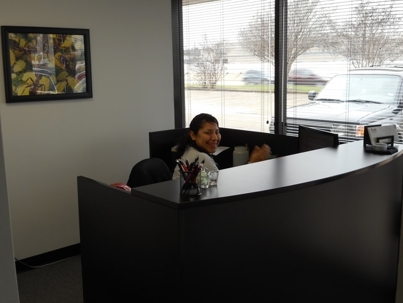 A smiling woman sits behind a dark, curved reception desk