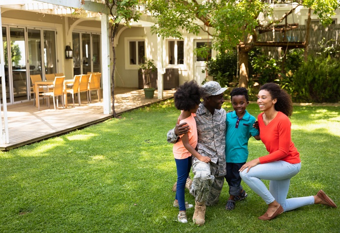 A Black soldier is reunited with his family on the lawn of their suburban home.